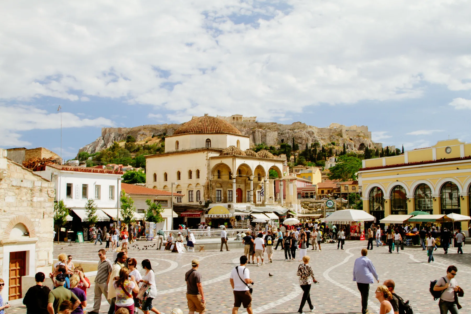 Monastiraki Square in Athens in daylight, with the domed old mosque, shops and the Acropolis rock rising behind the rooftops